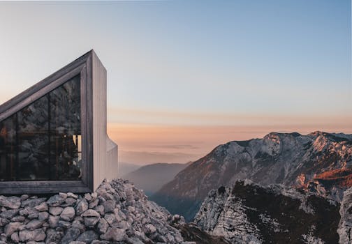 A sleek modern cabin perched on rocky terrains in Kranj, Slovenia, with stunning mountain views at sunset.