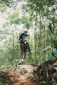 A dynamic shot of a biker performing a jump in a lush forest trail, showcasing extreme sport skills.
