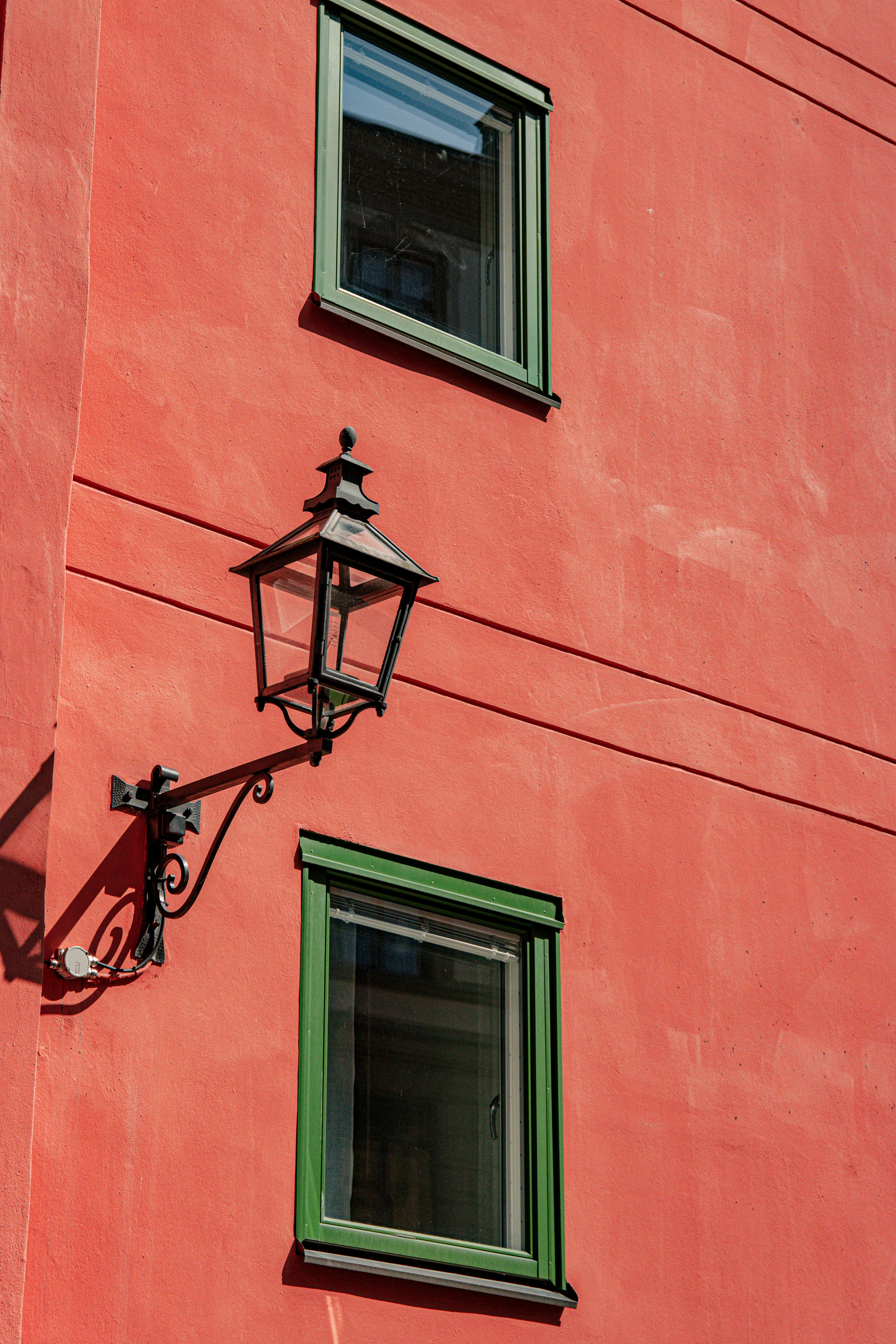 Vibrant red wall with two green framed windows and vintage lantern in Stockholm, Sweden.