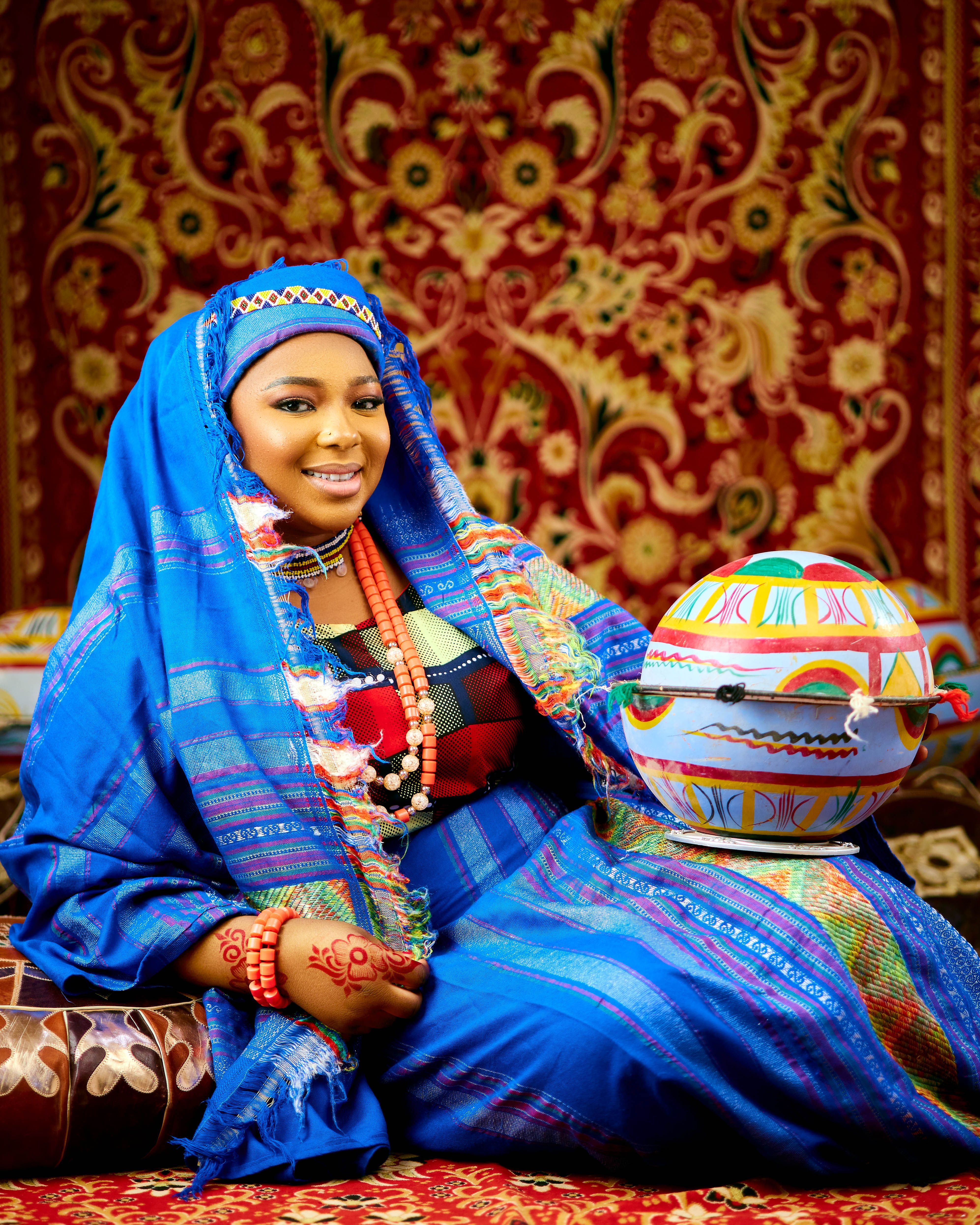 Woman in vibrant traditional attire holding a painted pot, smiling indoors.