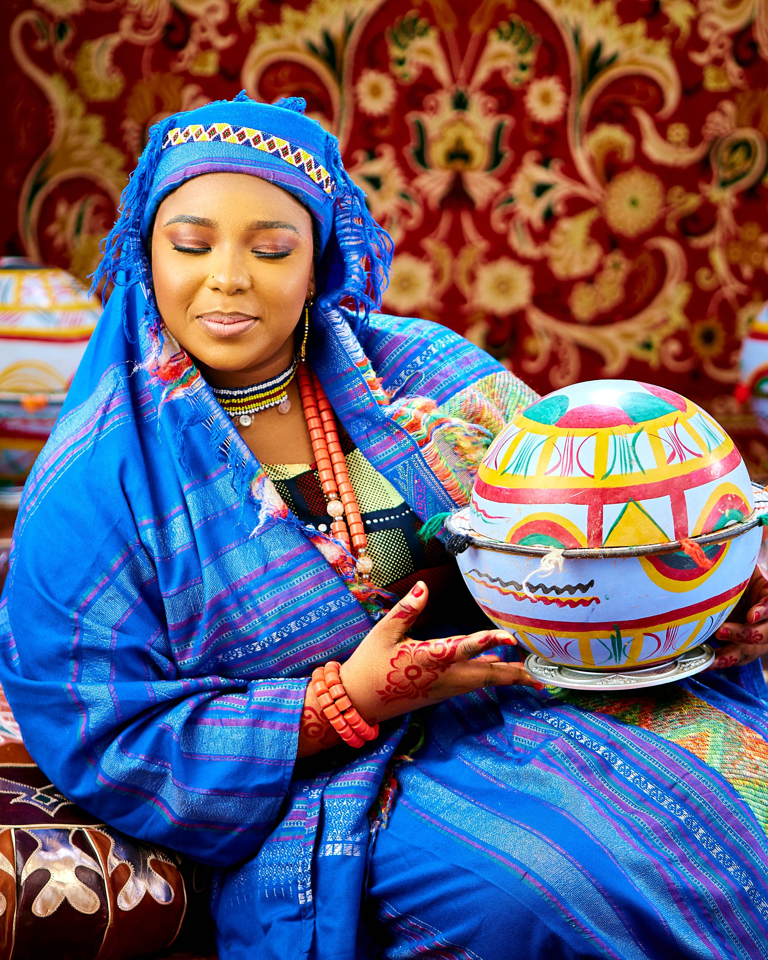 A woman in vibrant traditional attire holds a colorful painted pot, showcasing rich cultural heritage.