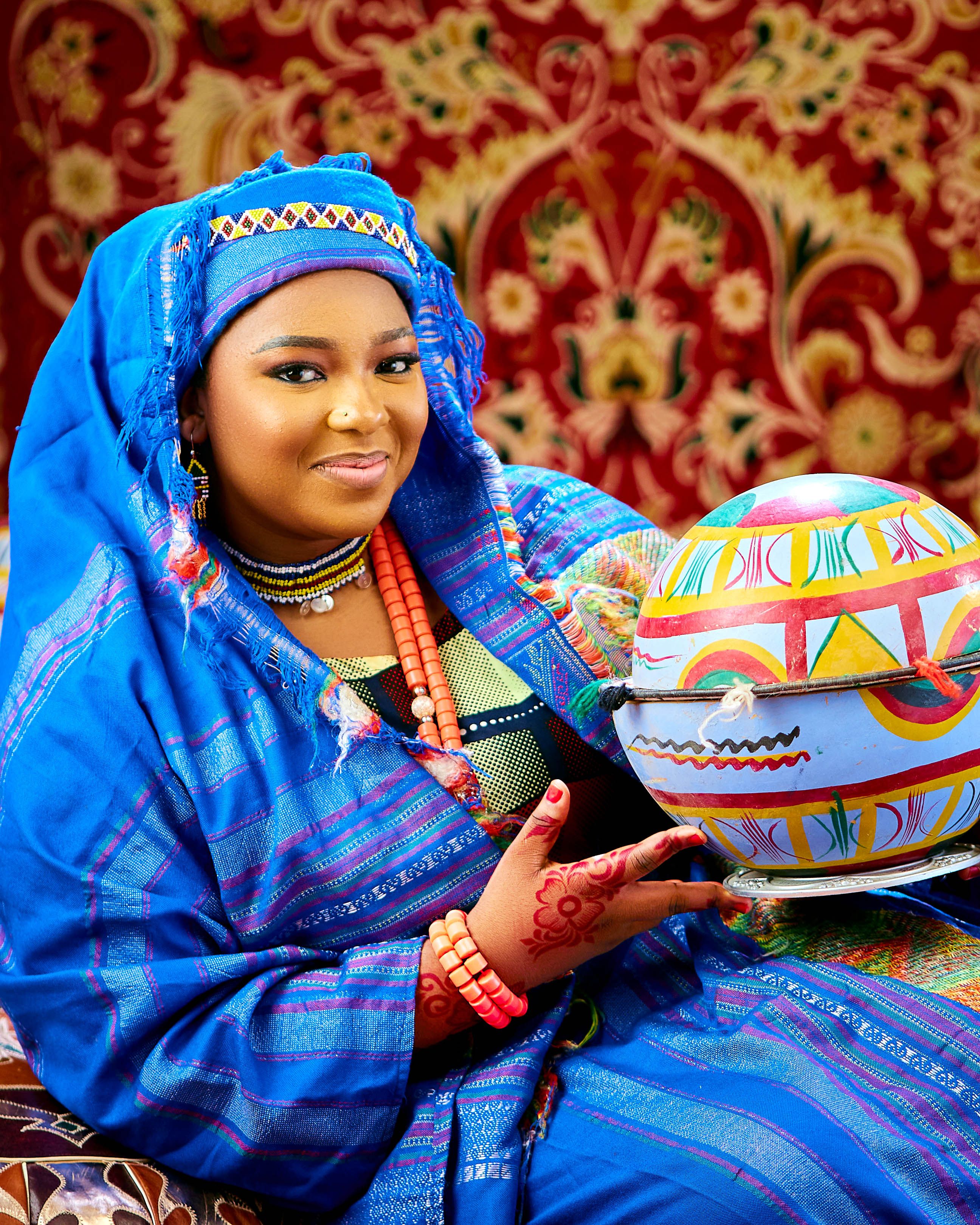Woman in vibrant traditional attire holding a decorated pot, showcasing cultural heritage.