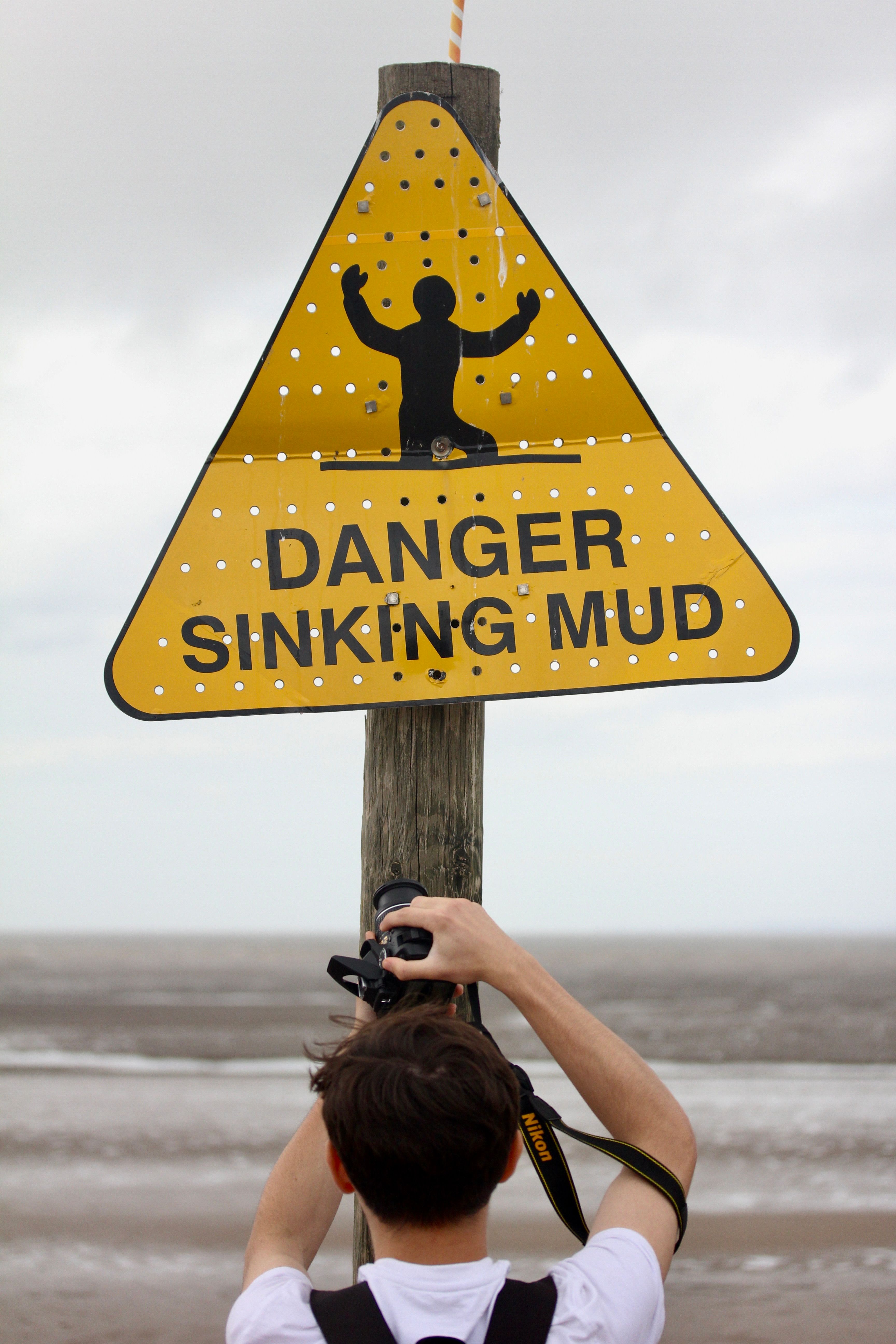Photographer captures a 'Danger Sinking Mud' sign on a cloudy beach.