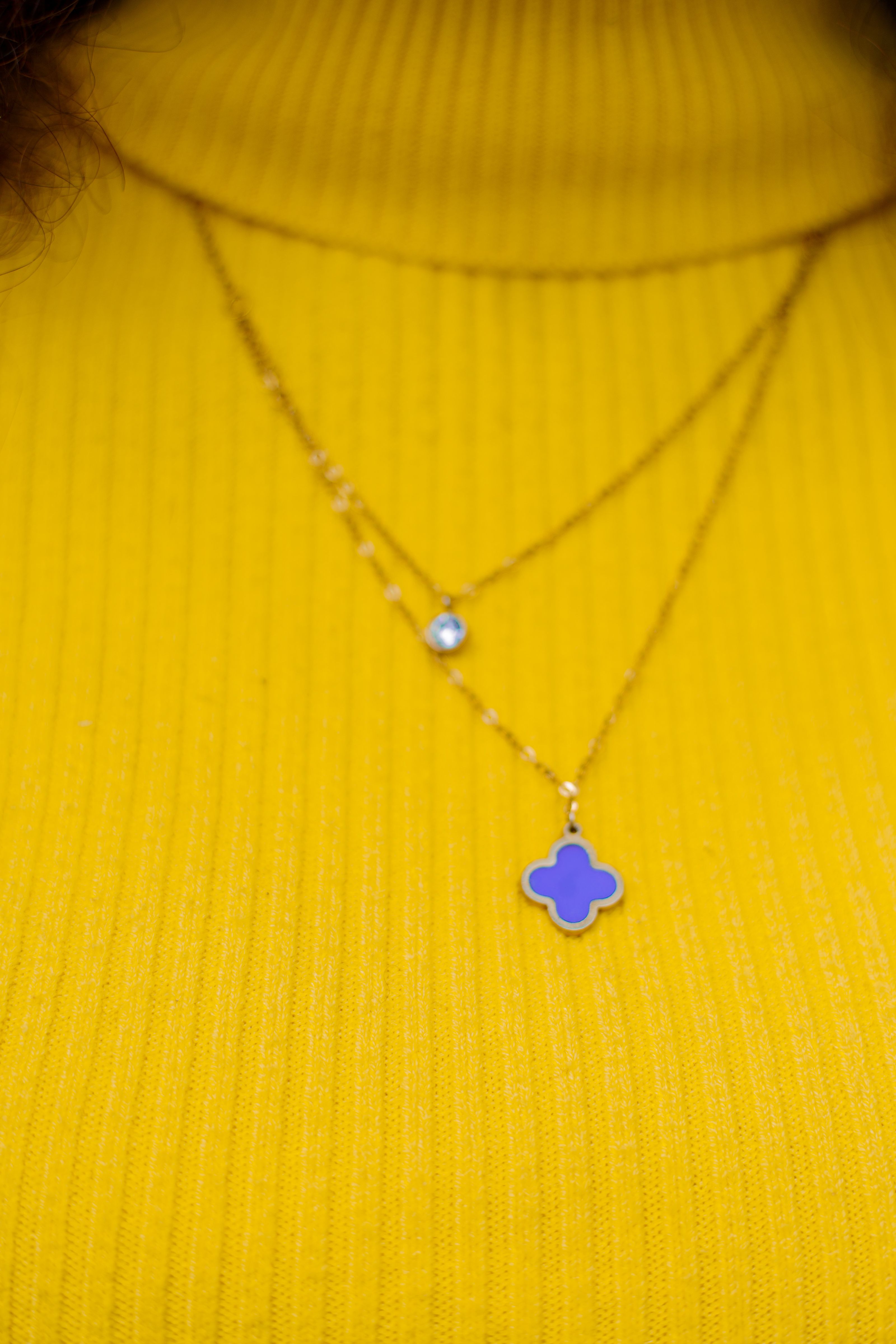 Close-up de um colar de ouro com um pingente roxo em um suéter canelado amarelo vibrante.