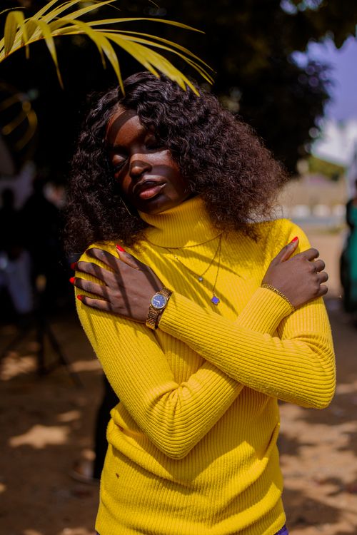 Free A fashionable woman in a yellow sweater poses gracefully outdoors, embracing herself. Stock Photo