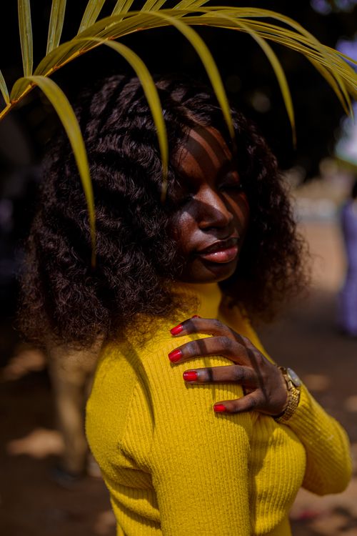 Free Portrait of a young woman in a yellow sweater under palm leaves, with natural lighting. Stock Photo