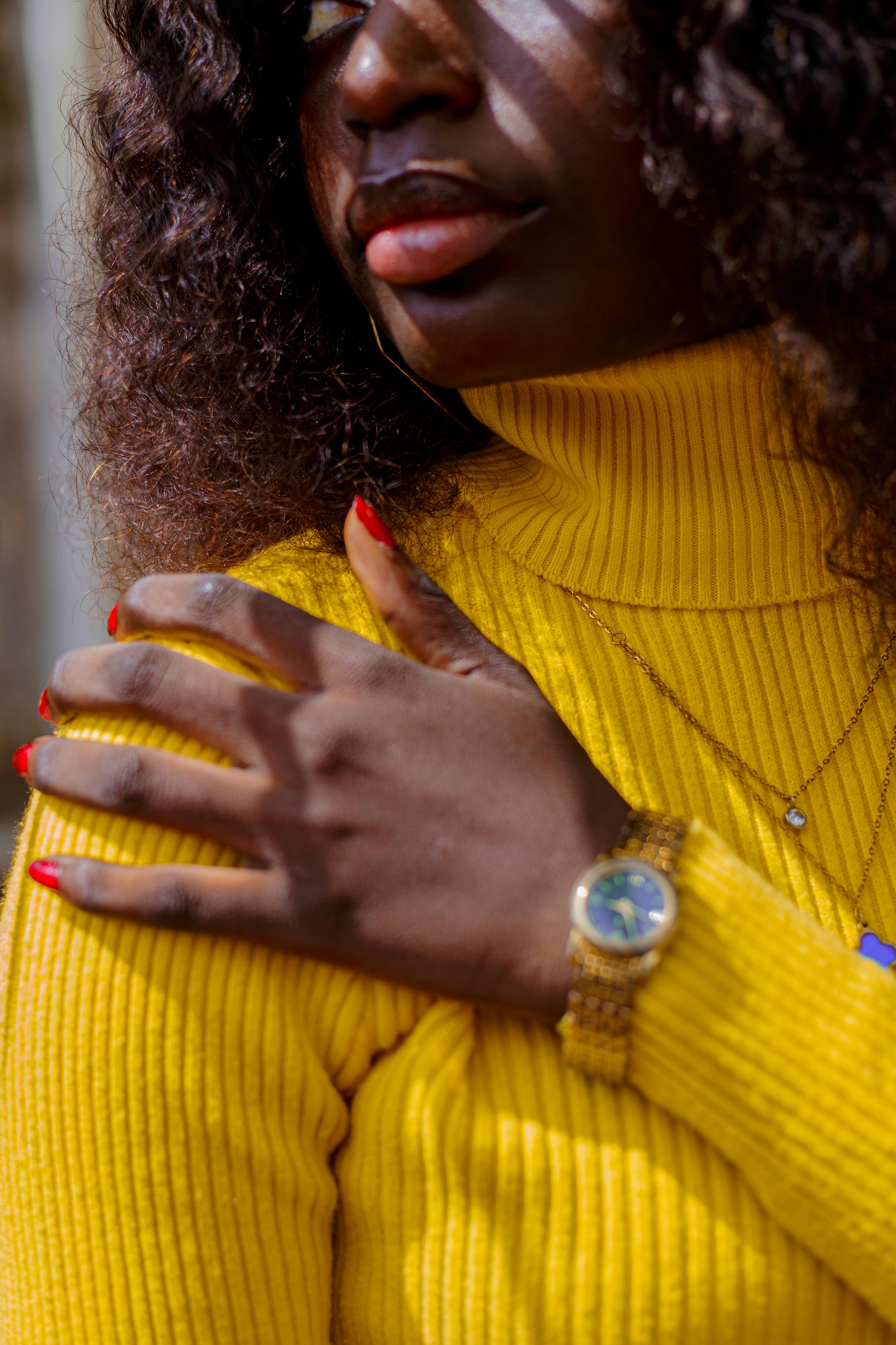 Portrait of a woman in a yellow turtleneck with red nails and a gold watch.
