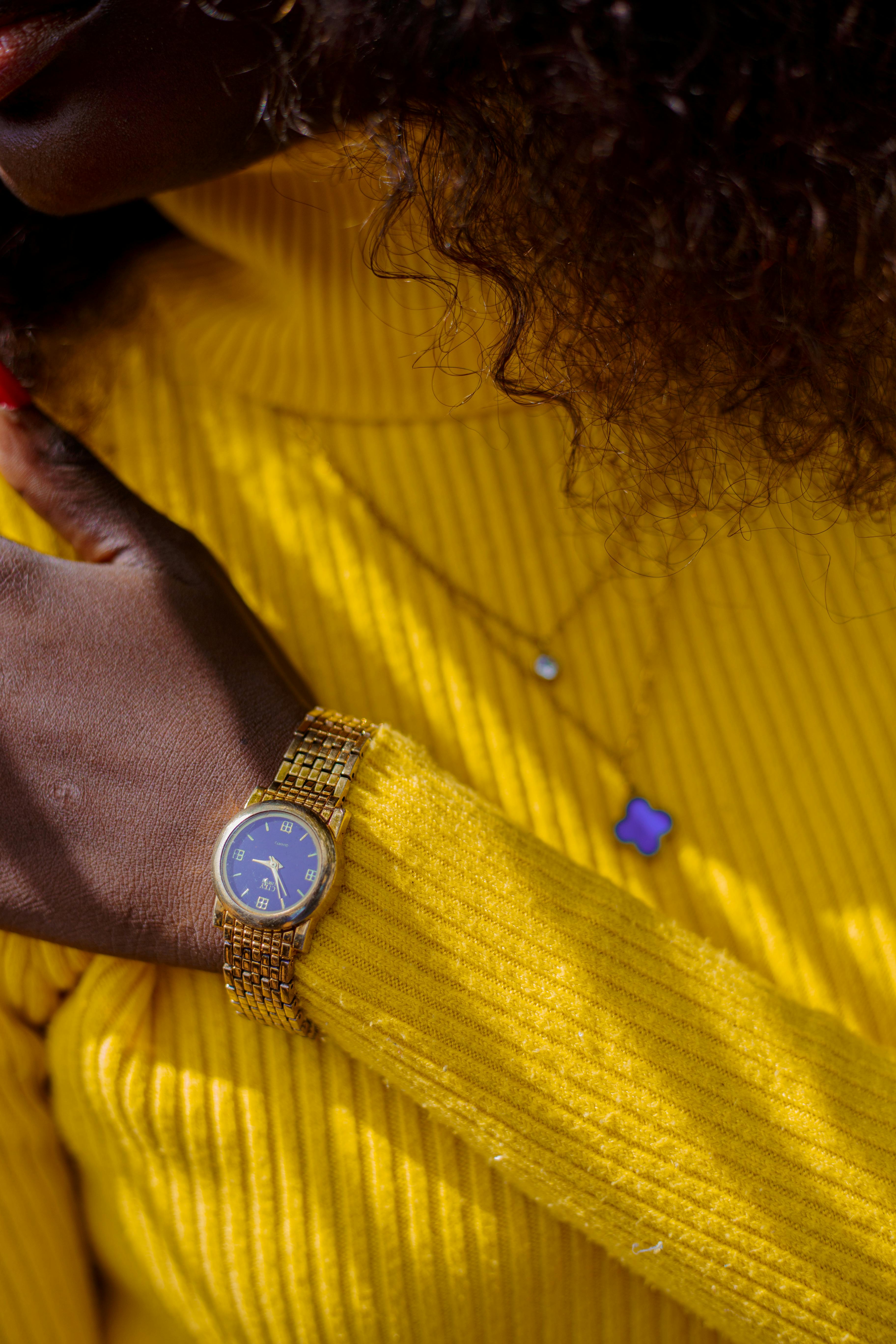 Close-up of a gold wristwatch on a person wearing a yellow sweater, evoking fashion and elegance.