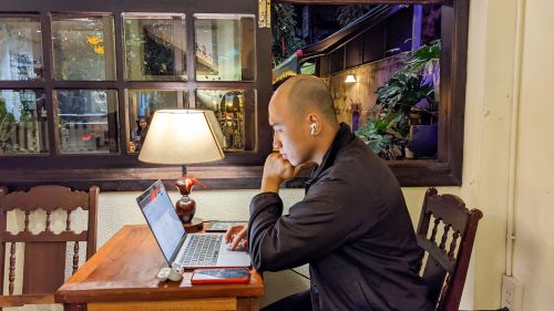 Free A person working on a laptop in a cozy Vietnamese cafe setting, creating a relaxed ambiance. Stock Photo