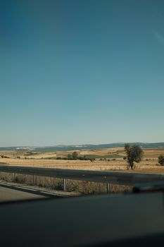 A serene countryside view from a moving car showing fields and distant hills under a clear blue sky.