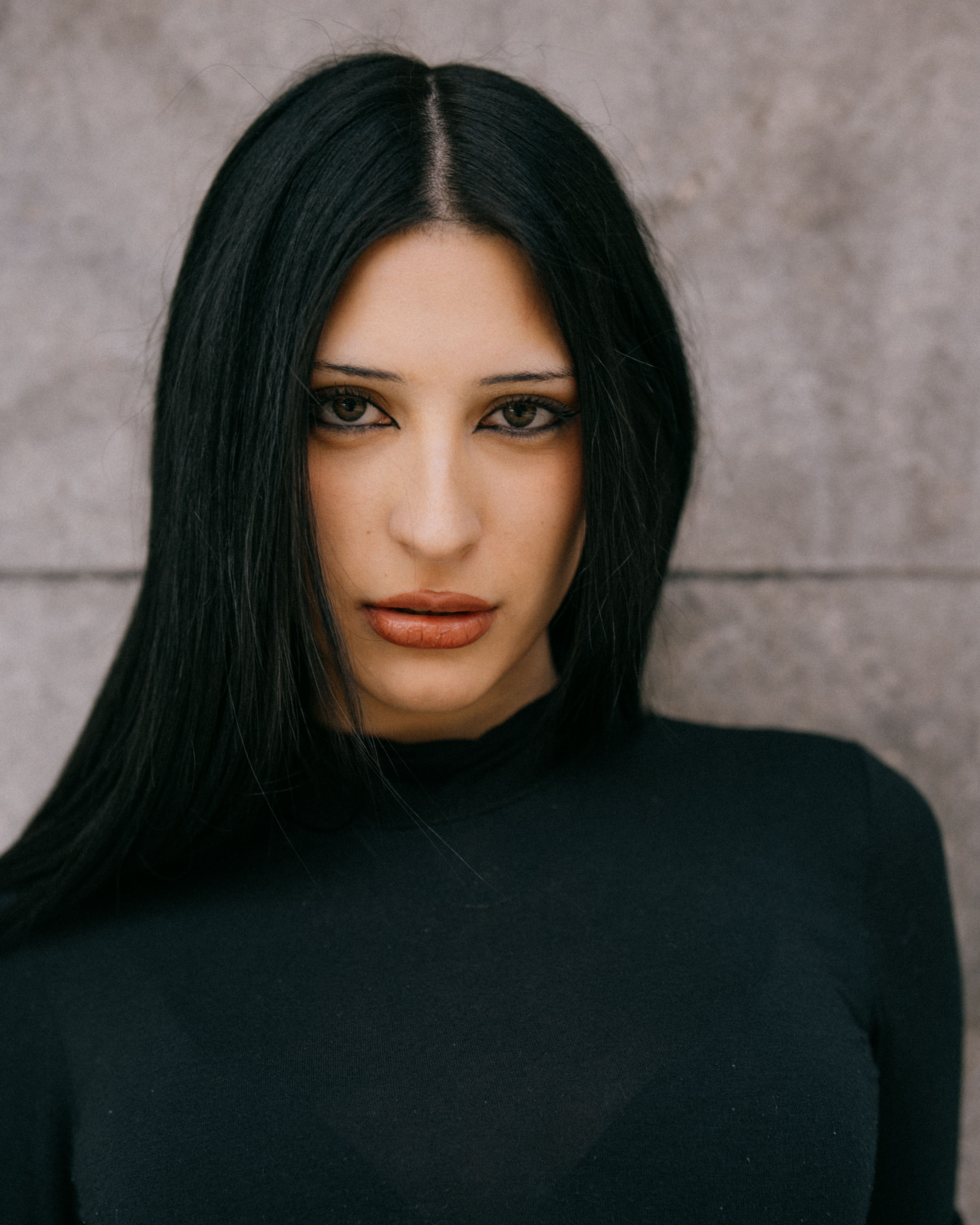 Close-up portrait of a woman with long black hair against a textured wall in Buenos Aires.