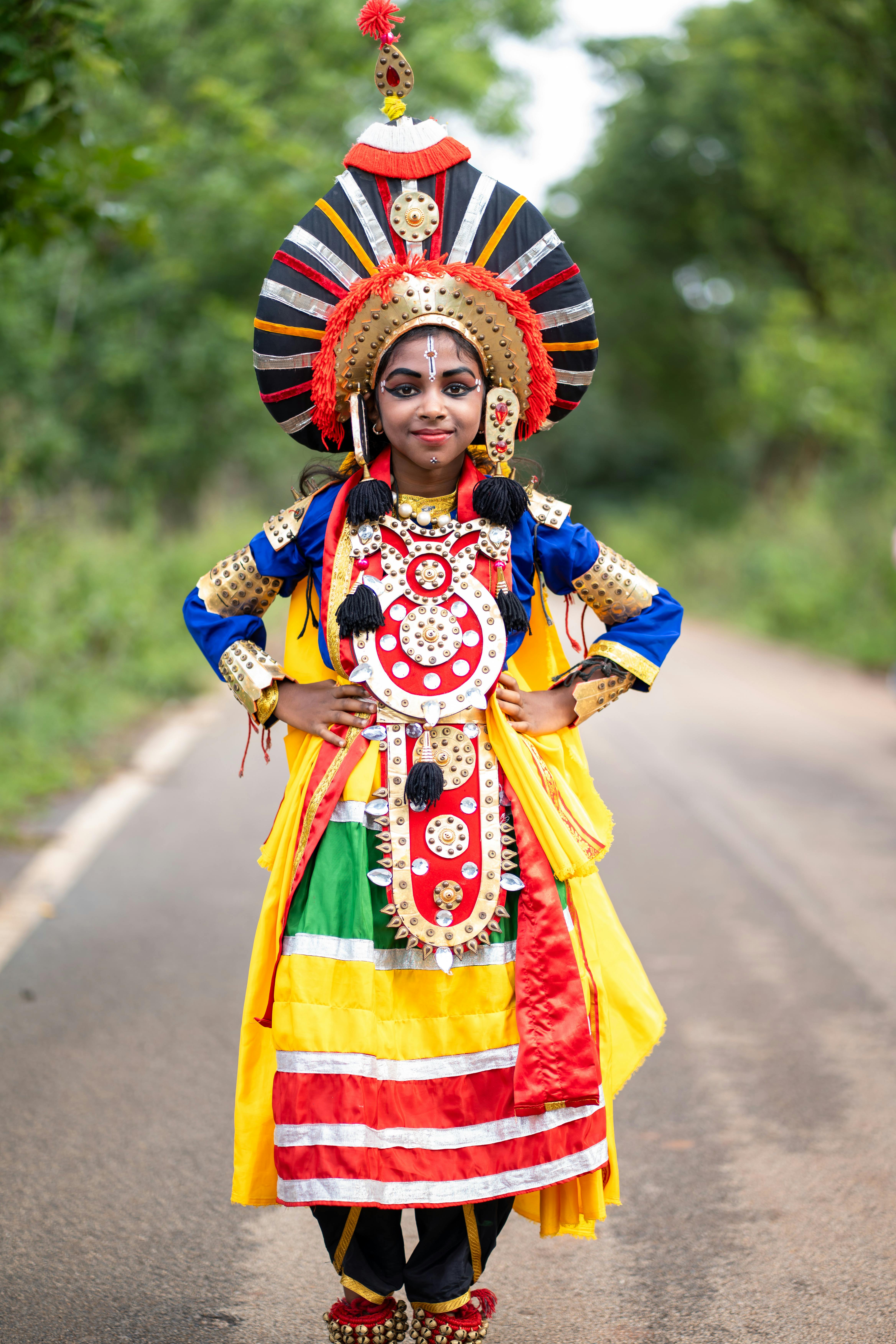 A person in vibrant traditional Indian dance attire poses outdoors on a road.