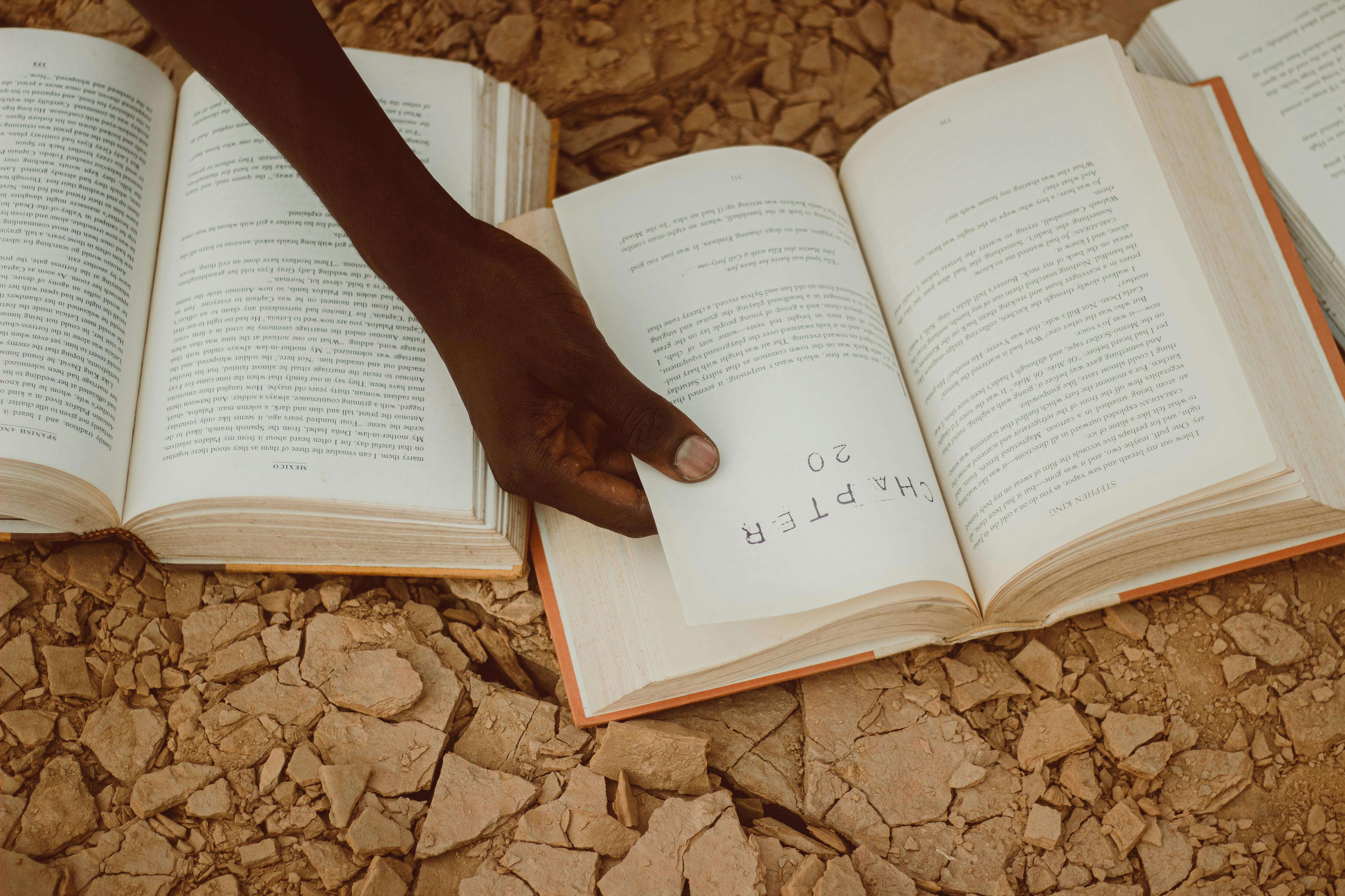 A person turning a page of a book set on a rocky surface, highlighting reading outdoors.