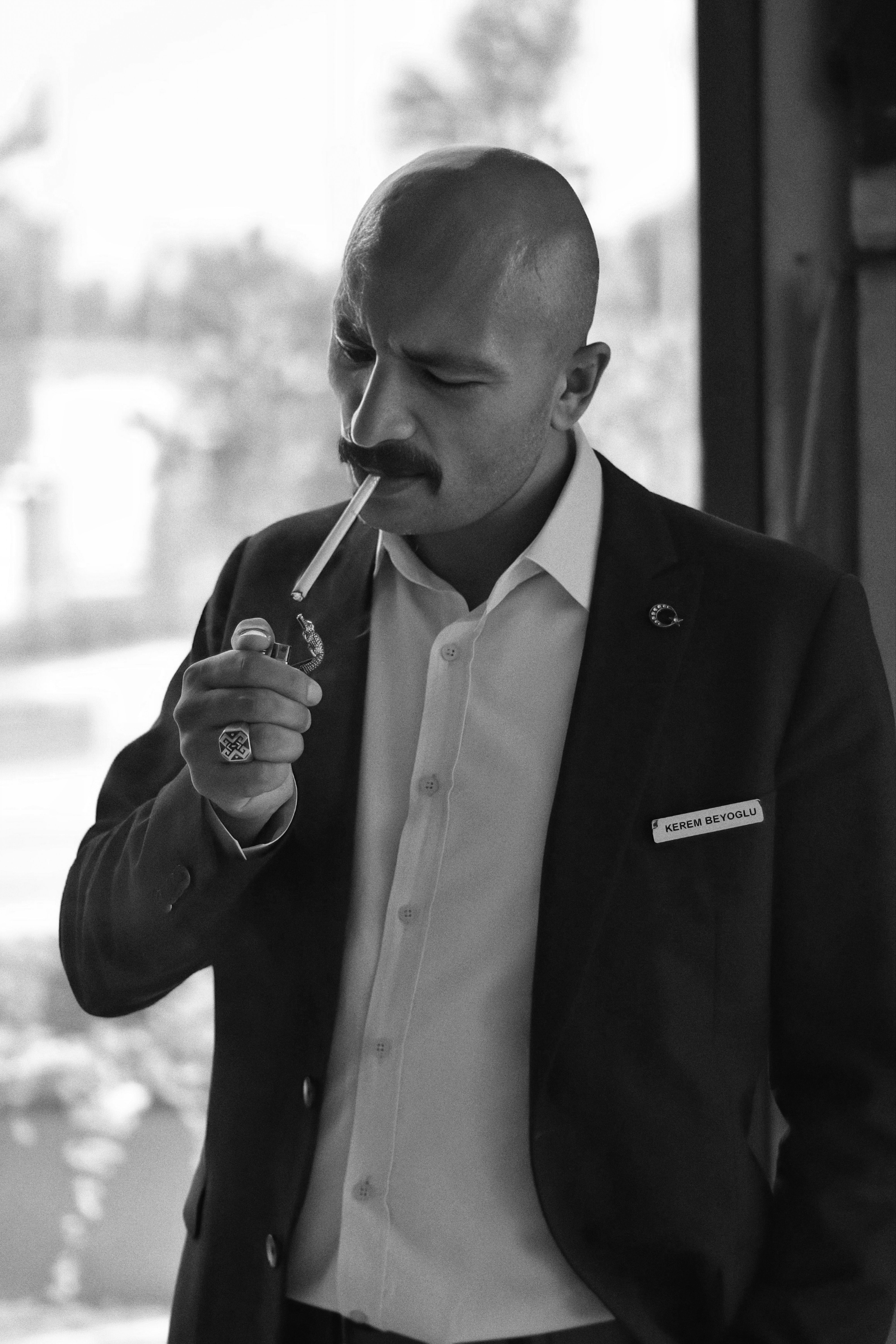Stylish man in suit lights pipe indoors, captured in classic monochrome.