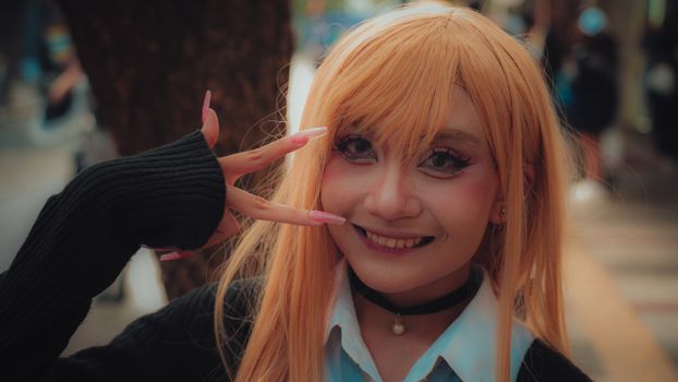 A vibrant cosplay portrait of a young adult in costume posing with a peace sign outdoors.