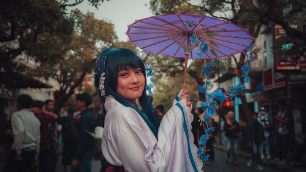 Cosplay performer in city street holding a vibrant purple parasol. Captivating contrast with cultural attire.