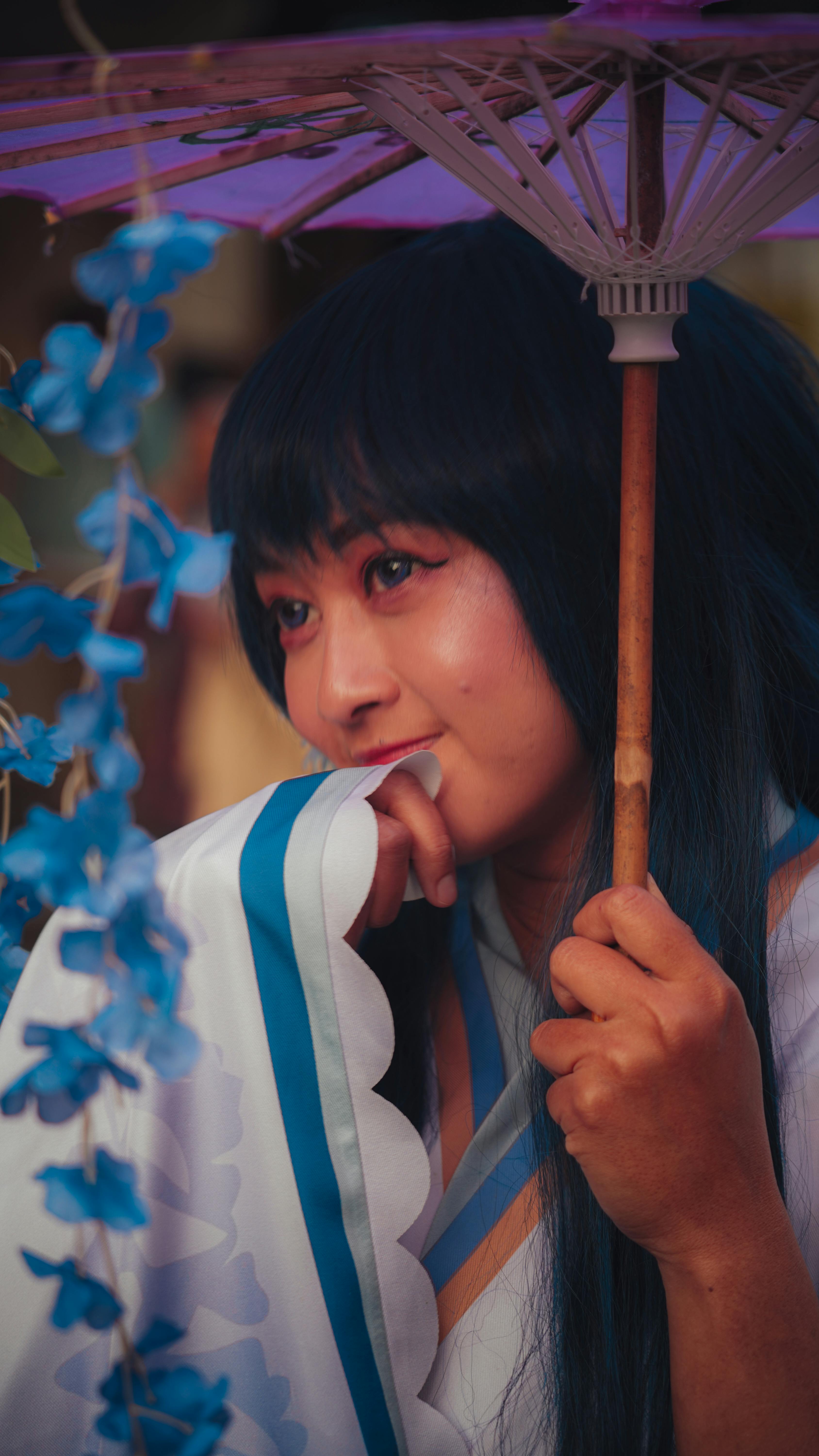 Asian woman in traditional dress with umbrella, surrounded by vivid blue flowers, creates a serene and cultural scene.