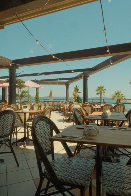 Free Charming outdoor cafe with view of ocean and palm trees, perfect for summer relaxation. Stock Photo