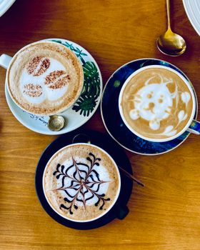 Three beautifully crafted latte art designs on cappuccinos in a cozy cafe setting.