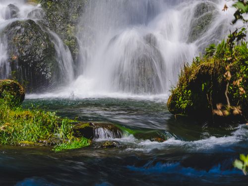 Free A tranquil waterfall cascading over rocks surrounded by lush greenery. Stock Photo