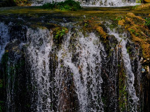 Free A mesmerizing view of a cascading waterfall with vibrant greenery around, captured during a sunny day. Stock Photo