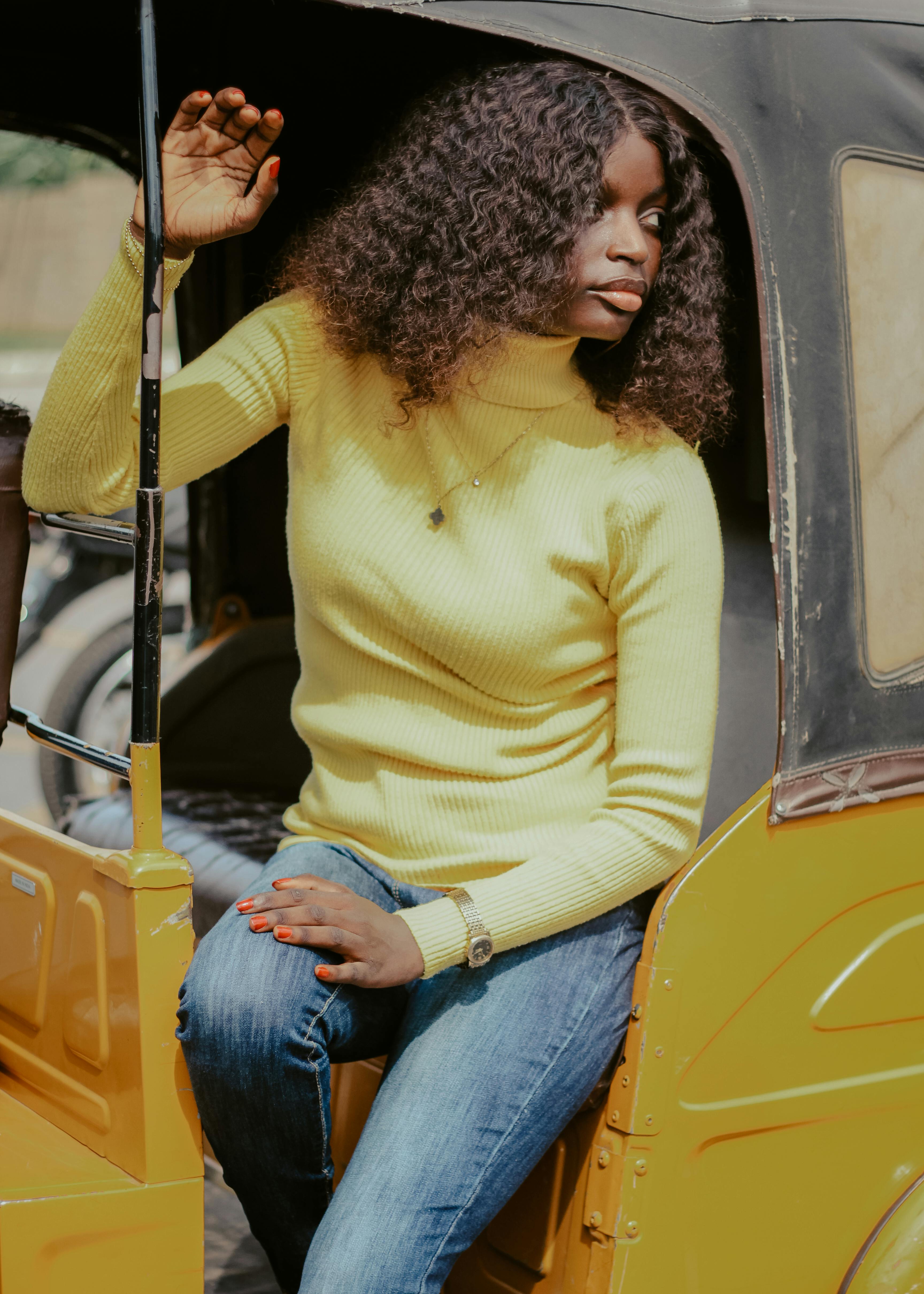 Free Stylish young woman wearing a yellow sweater and jeans sitting in a yellow rickshaw, looking contemplative. Stock Photo