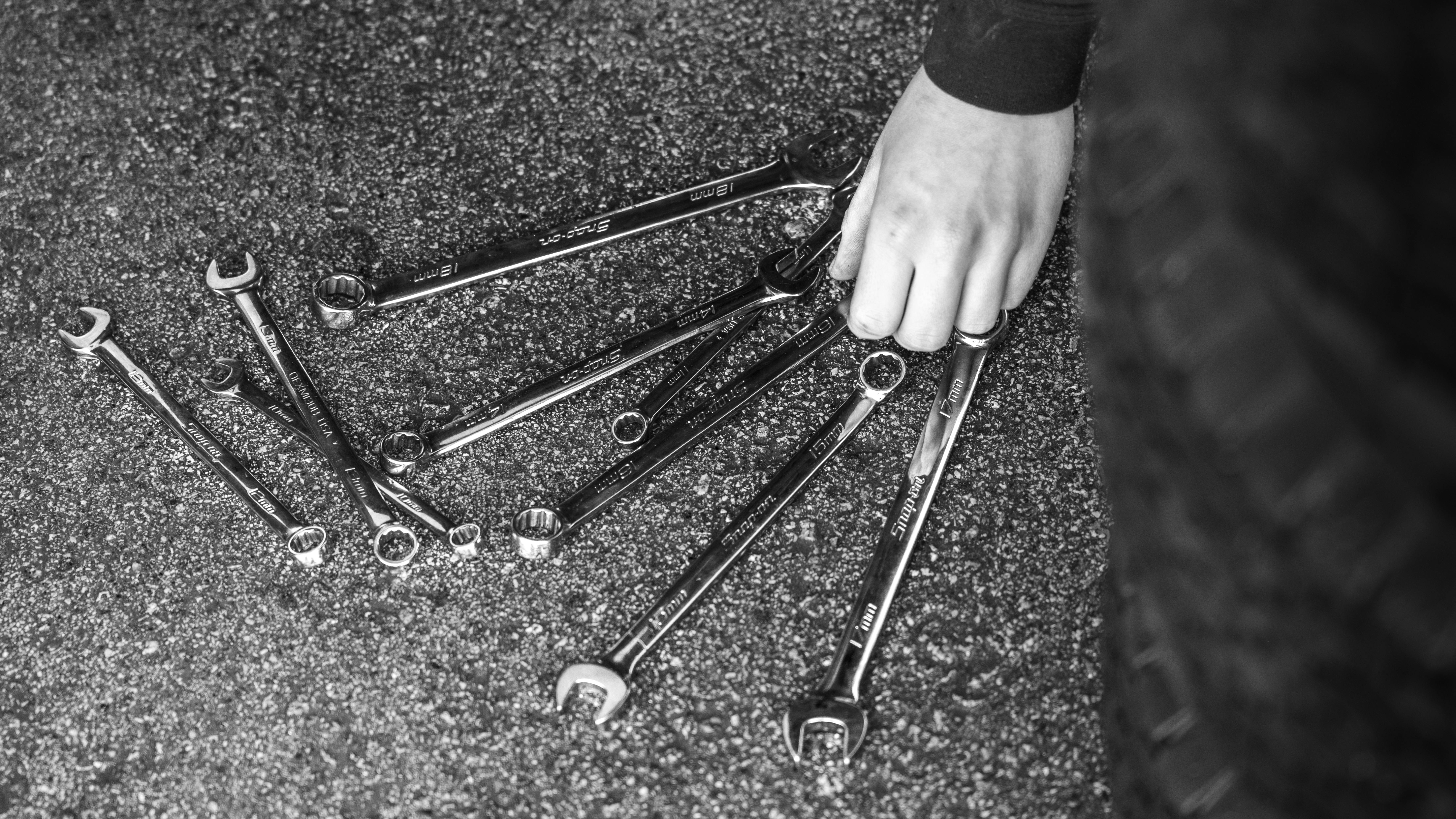 Miễn phí Hình ảnh đen trắng về những chiếc cờ lê trải trên nhựa đường với một bàn tay đang nhặt một chiếc. Ảnh lưu trữ