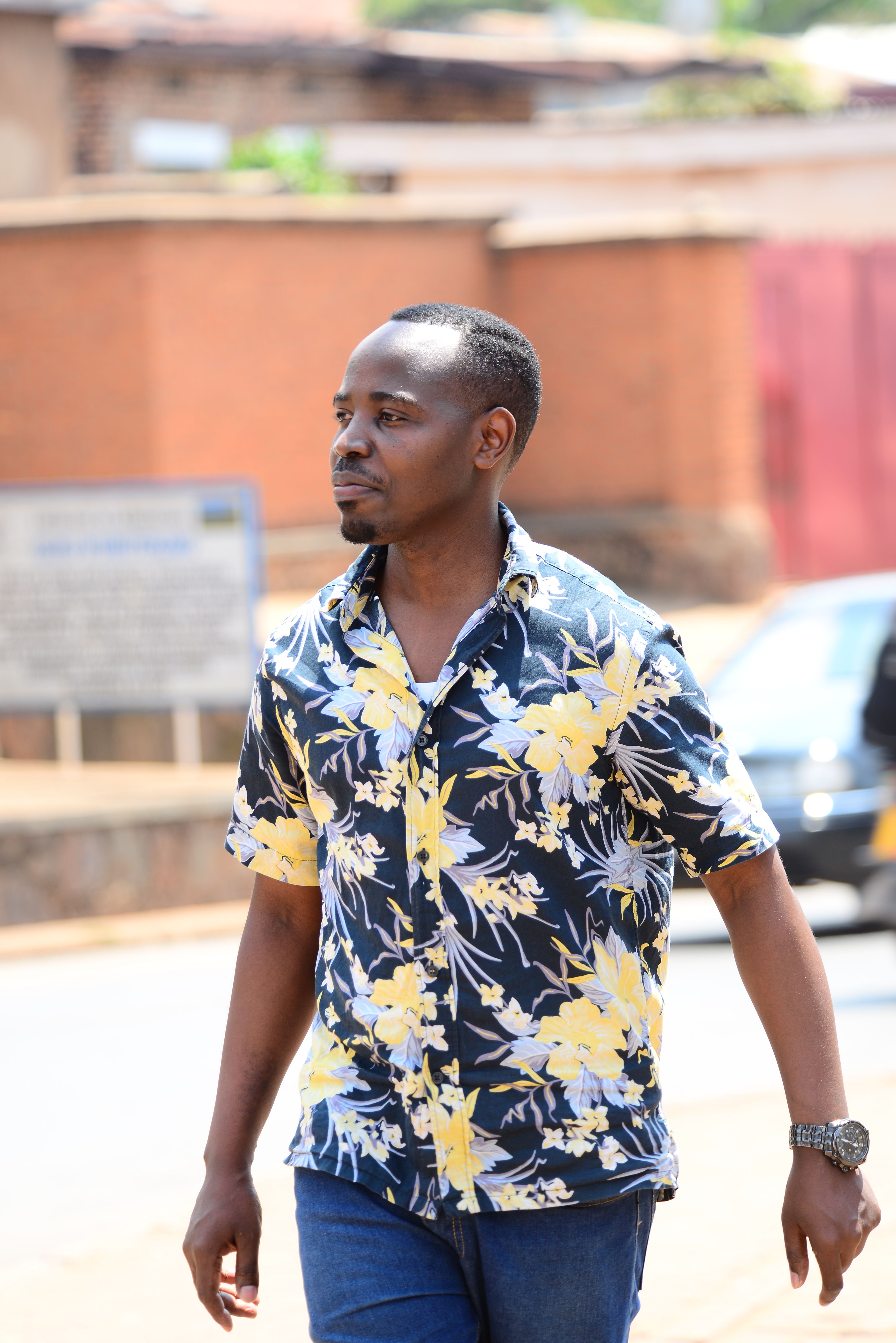 Casual man in floral shirt walking casually on a sunny urban street.