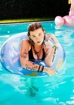 A stylish tattooed model in a pool float enjoying a sunny day by the pool.