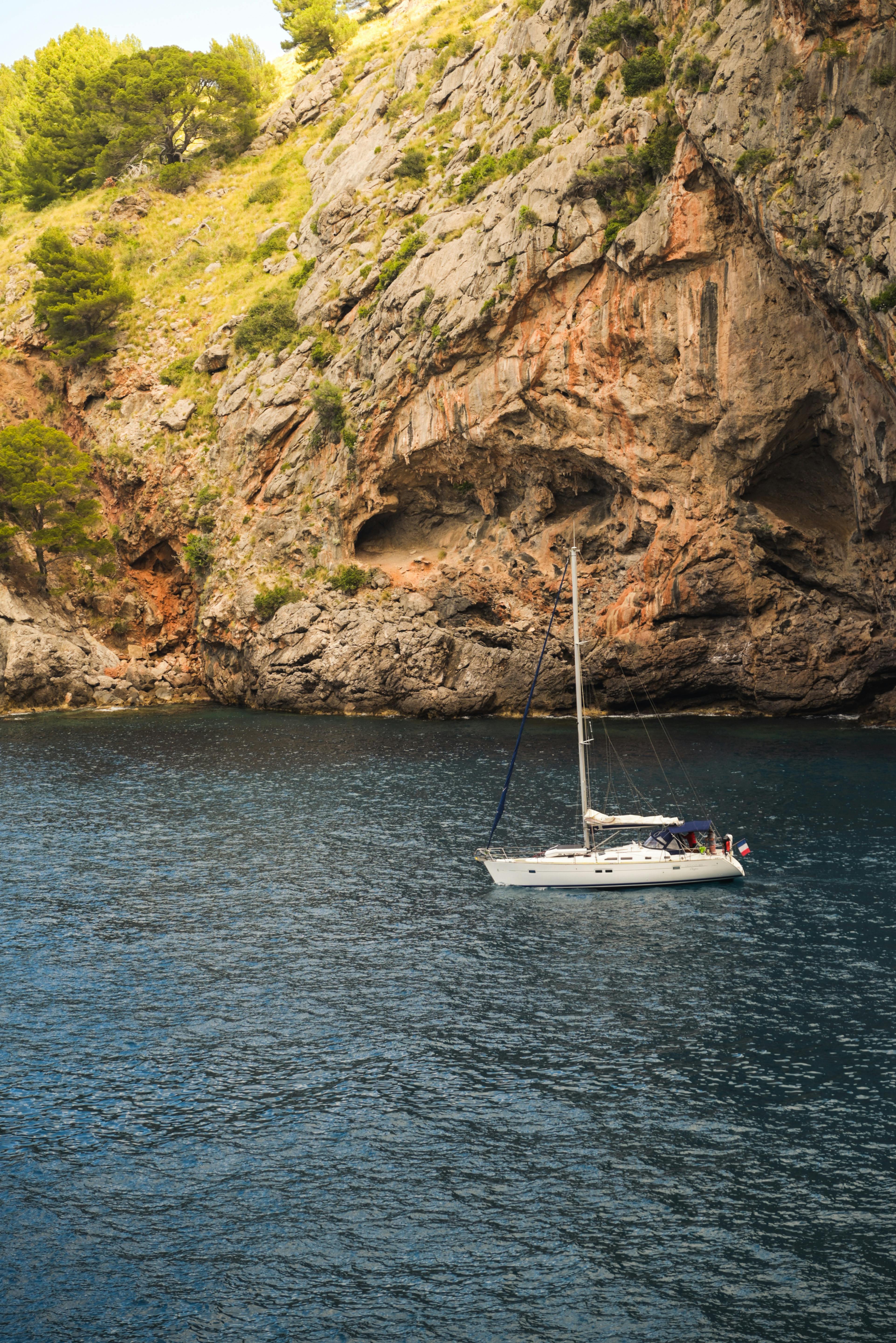 Serene sailboat anchored by rocky cliffs in Mallorca, Balearic Islands.
