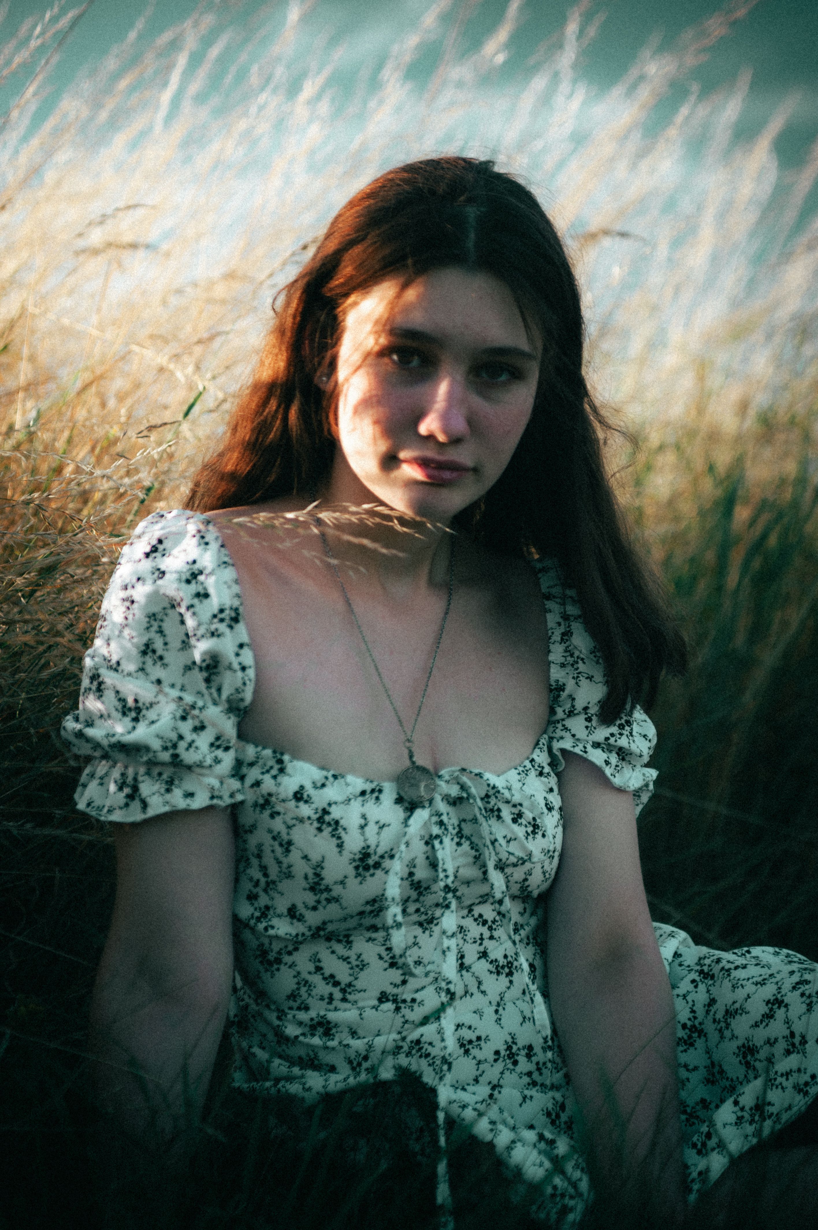 Moody portrait of a young woman sitting in a Ukrainian field during golden hour.