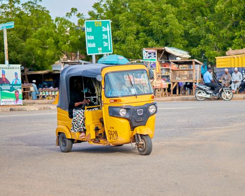 Free A yellow tuk-tuk rides through a busy street filled with local life in an African town. Stock Photo