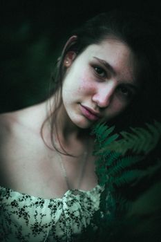 A captivating portrait of a woman surrounded by ferns, evoking a dark, moody atmosphere.