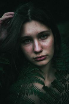 Moody portrait of a woman surrounded by lush ferns in a dark forest setting.
