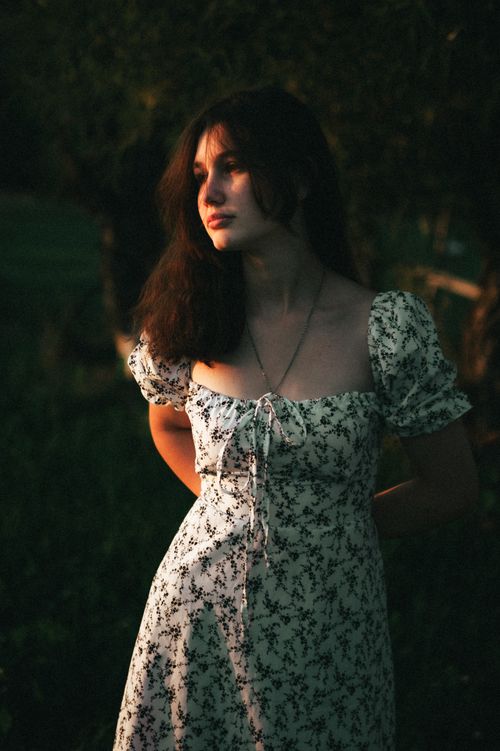 Free A young woman in a vintage floral dress enjoys the serene sunset outdoors. Stock Photo