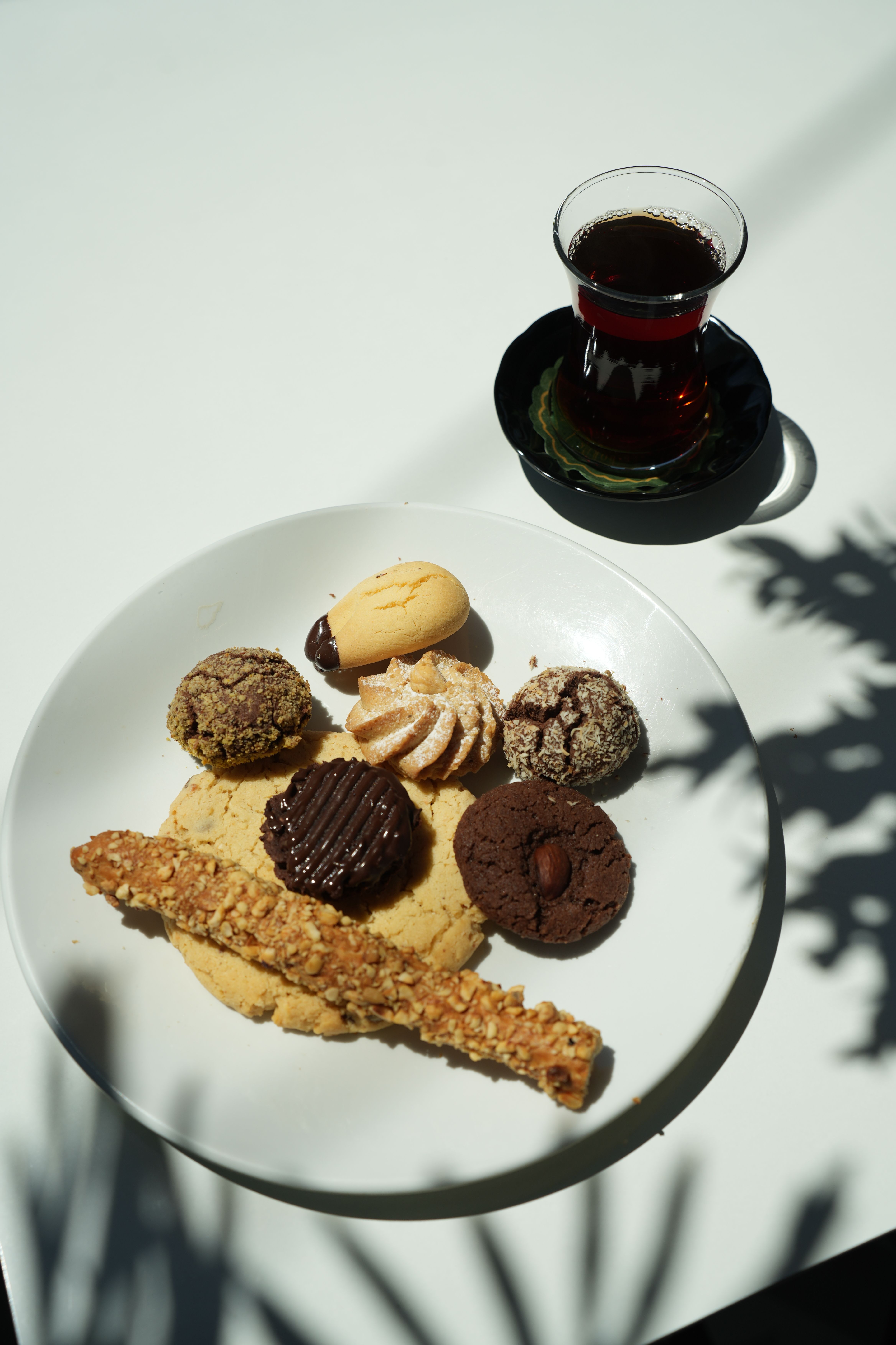 A variety of cookies served on a white plate with Turkish tea on a sunny table setting.