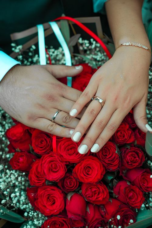 Free Close-up of couple's hands with wedding rings over a bouquet of red roses, symbolizing love and commitment. Stock Photo