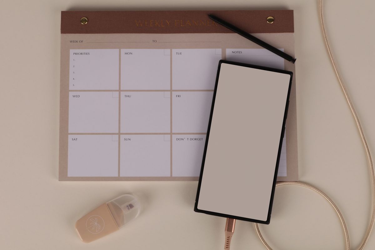 Meja kerja modern dengan planner mingguan smartphone dan alat tulis untuk prioritas task harian