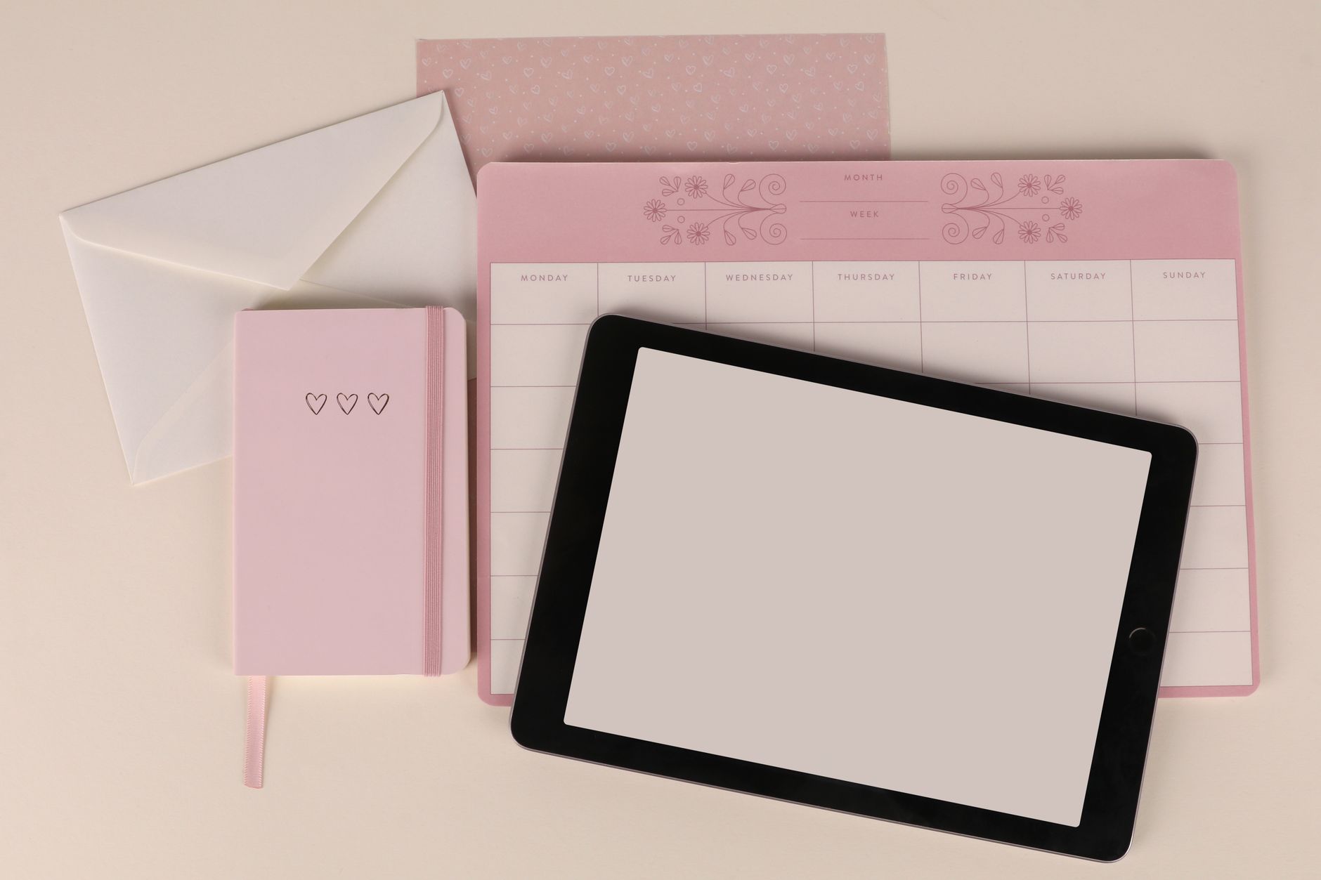 Flat lay of a pink planner, envelope, and tablet on a desk, perfect for organization themes.
