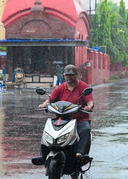 A man rides a scooter through a wet street during a rainfall, India.