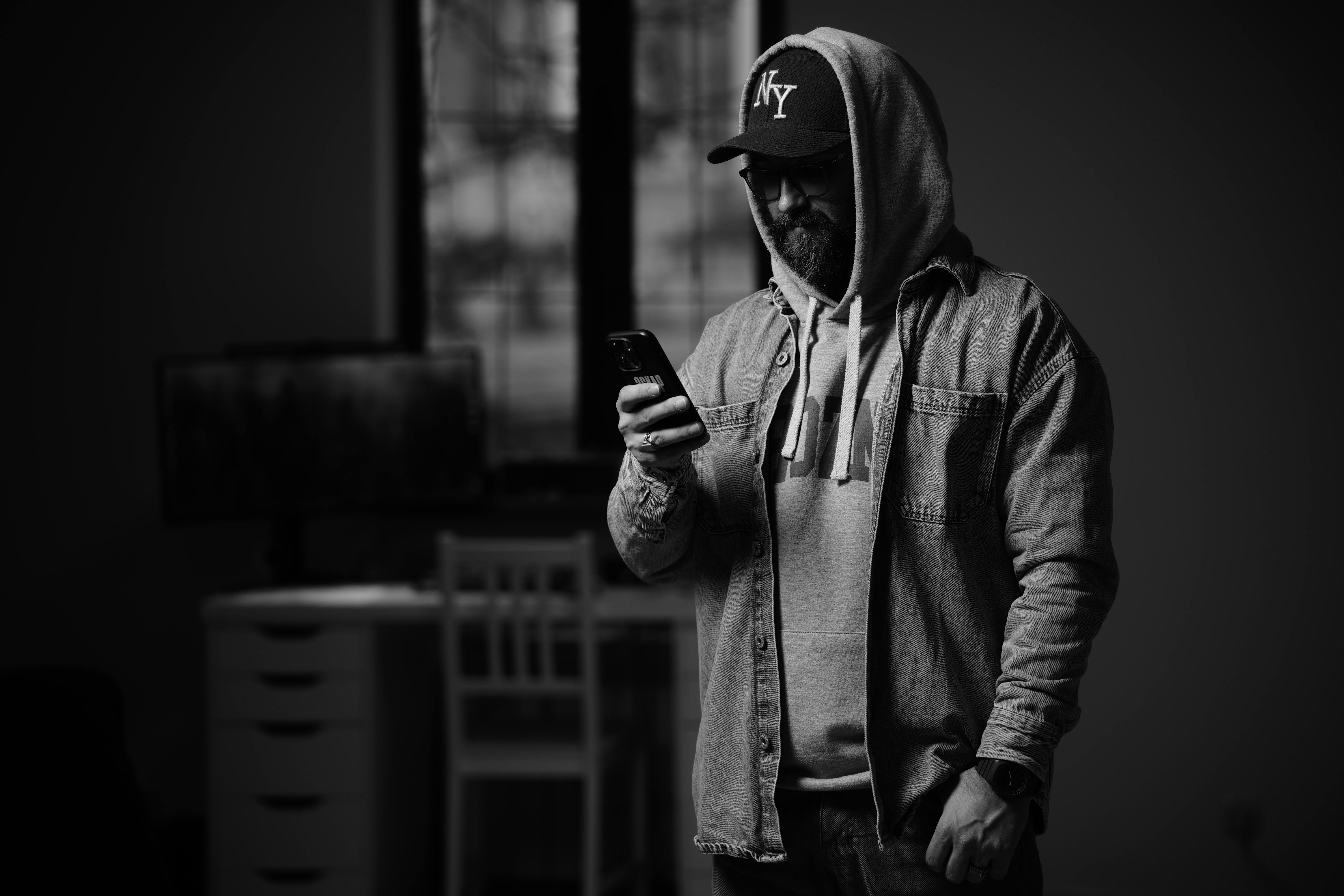 Free Bearded man in hoodie using smartphone in dark room, stylish and modern Stock Photo