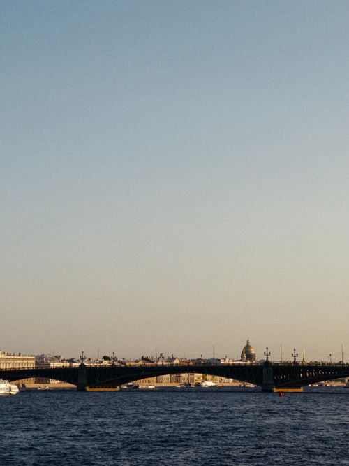 Free Tranquil sunset view of a historic bridge over a calm river with city skyline. Stock Photo