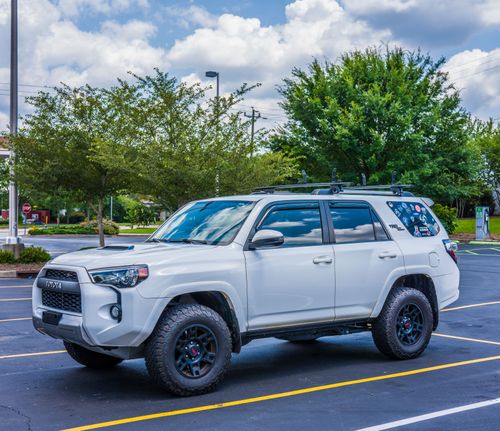 Free White SUV parked in an outdoor lot with trees and cloudy sky in the background. Stock Photo