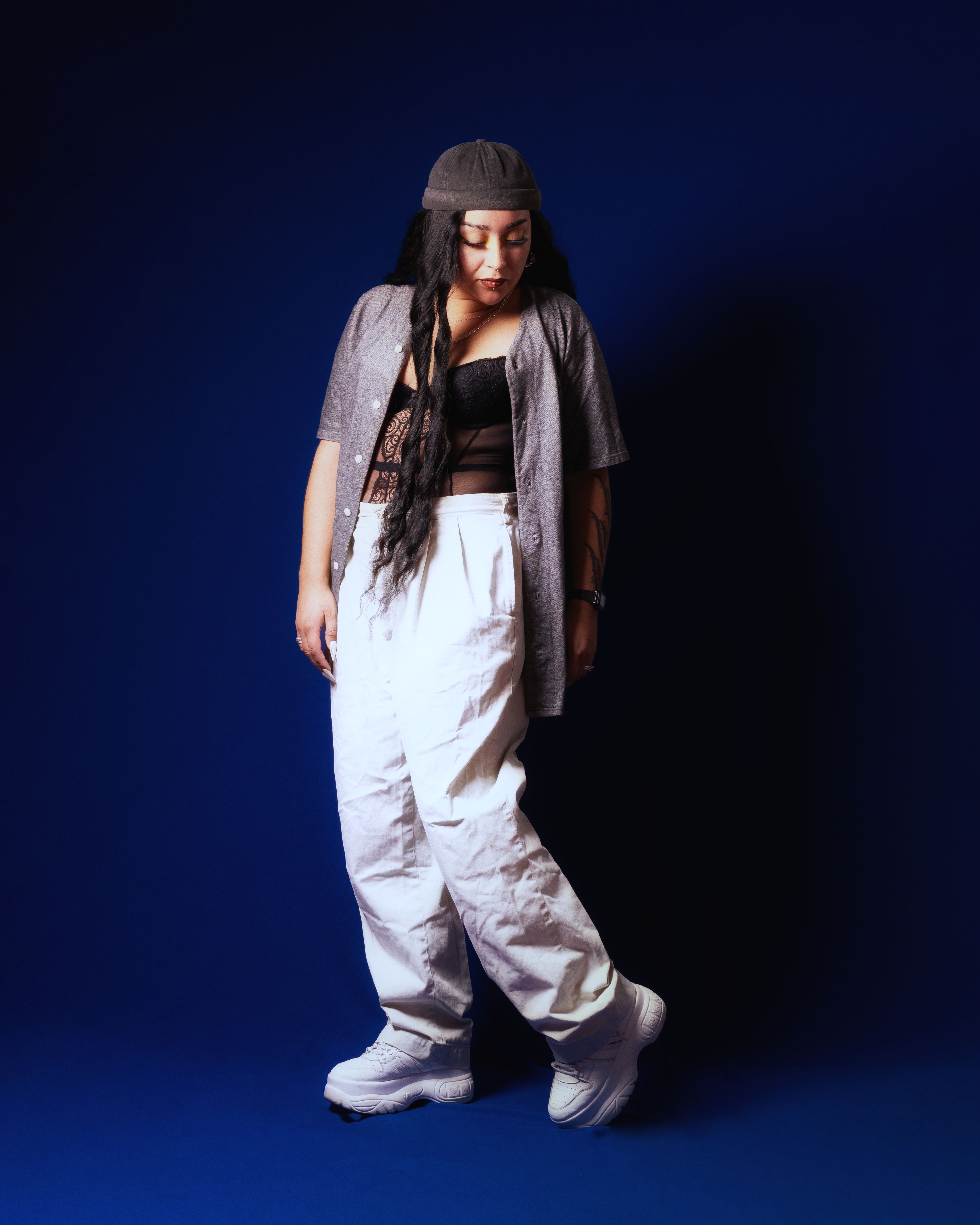 Fashion-forward woman in urban street style outfit posing against a vibrant blue backdrop.