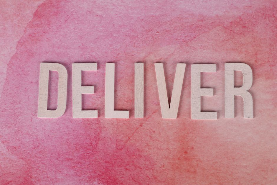 ビジネスコンセプトのためのピンクのテクスチャ背景に「Deliver」と綴る木製の文字。