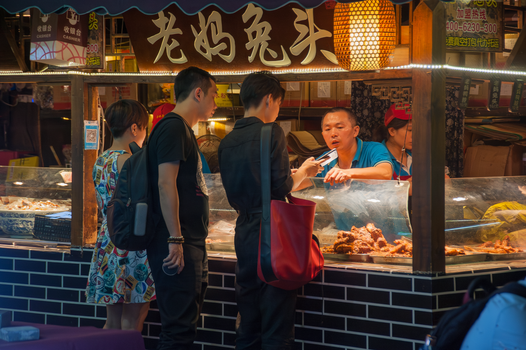 Street food stall with people ordering in a bustling Asian night market.