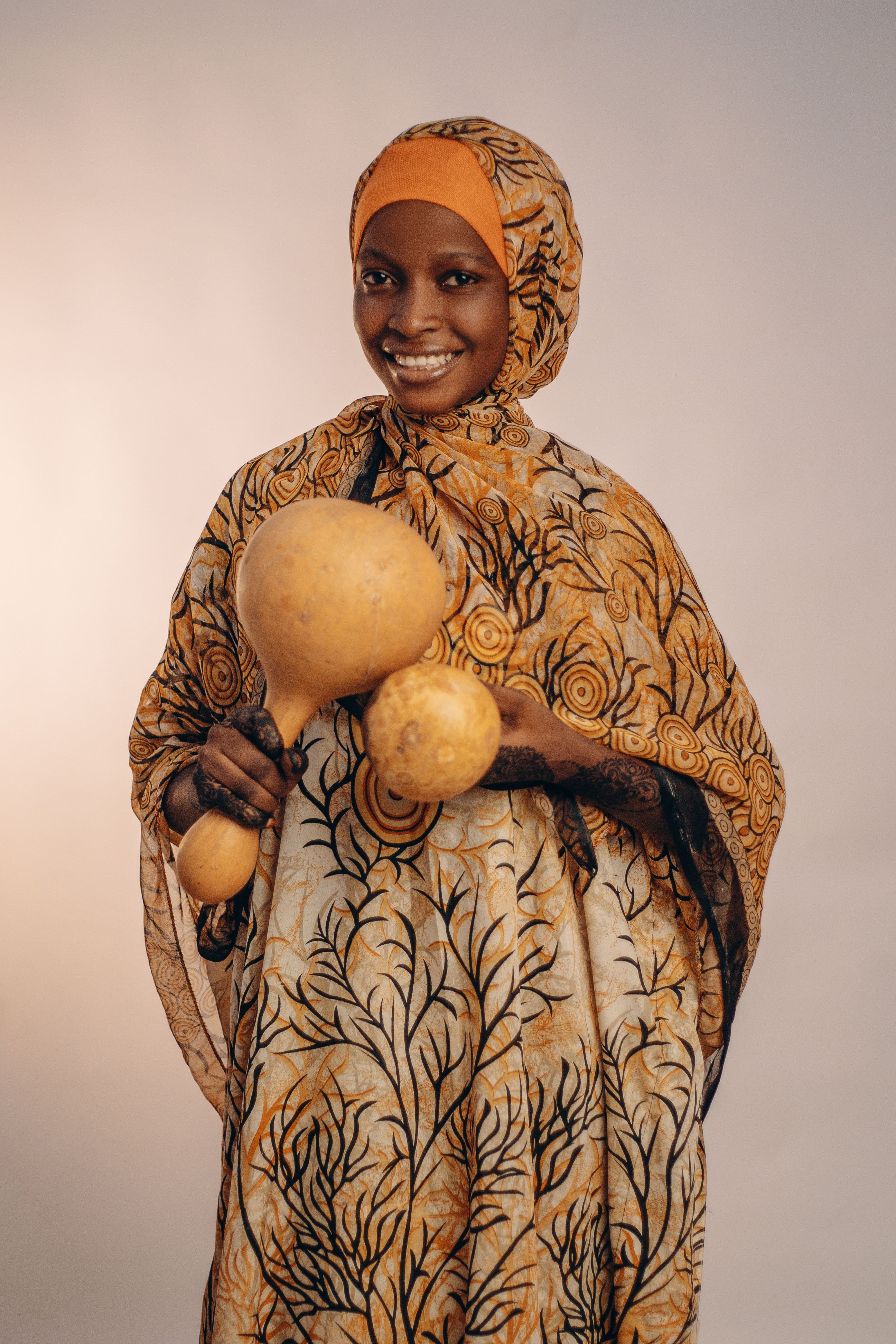 A smiling woman in traditional African attire holds decorative gourds, showcasing cultural elegance.