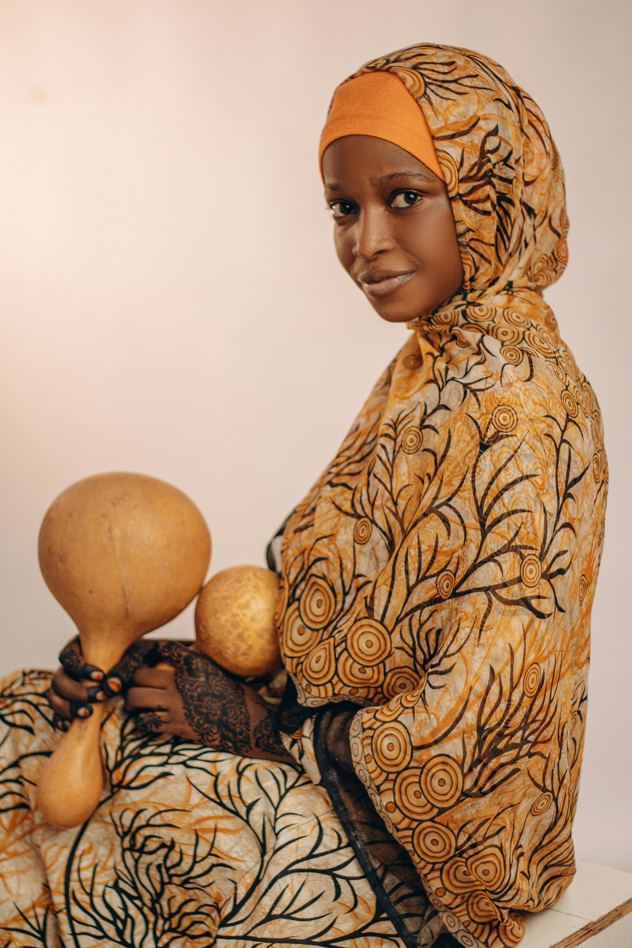 Graceful woman in traditional patterned clothing holds decorative gourds, exuding cultural elegance.