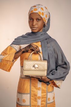 Stylish woman in colorful traditional dress holding a designer handbag. Studio portrait.