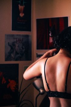Artistic indoor portrait featuring a woman adjusting top, surrounded by art posters.